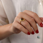 Hand wearing a gold ring with a  gemstone against a neutral background