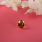 Gold ring with a brown gemstone on a pink background with white flowers.