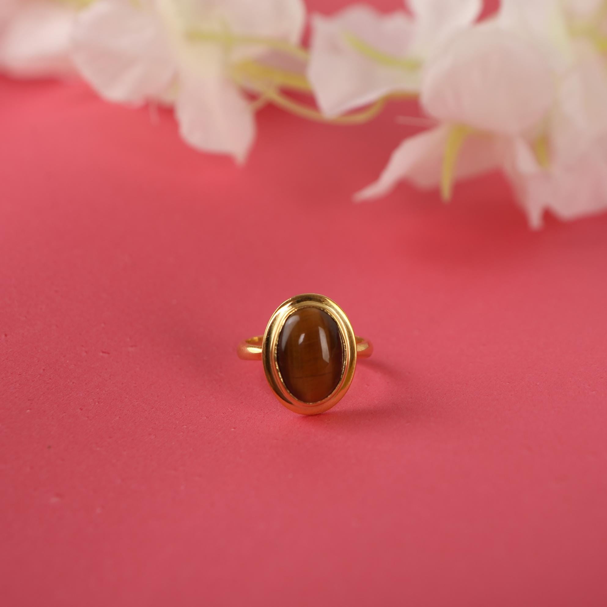 Gold ring with a brown gemstone on a pink background with white flowers.