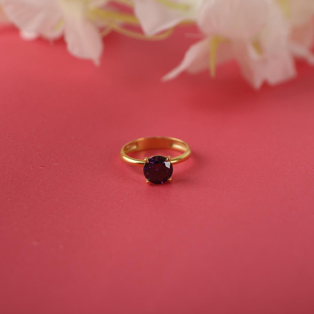 Gold ring with a purple gemstone on a pink background with flowers.