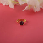 Gold ring with a purple gemstone on a pink background with flowers.