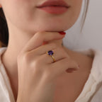 Close-up of a hand wearing a gold ring with a purple gemstone, touching the chin.