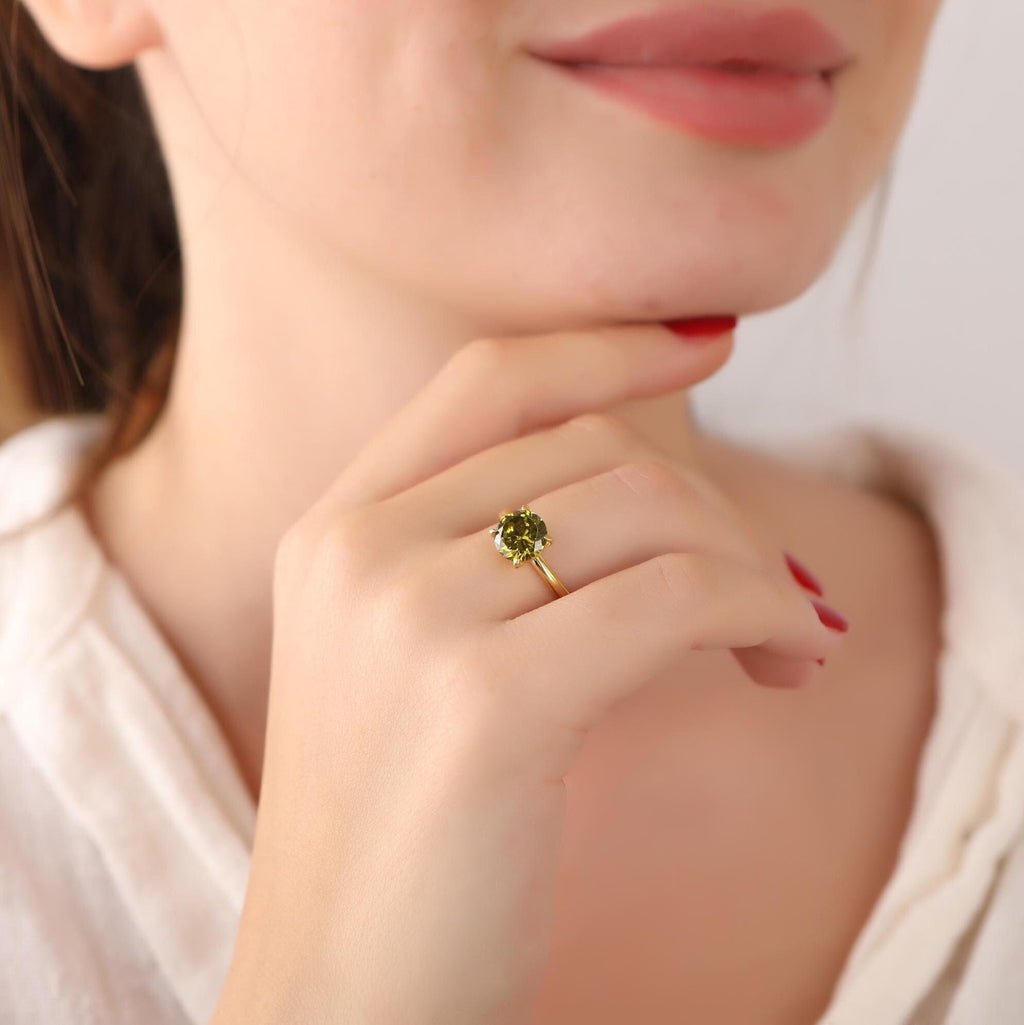 Close-up of a woman's hand wearing a gold ring with a green gemstone, touching her chin.