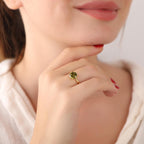 Close-up of a woman's hand wearing a gold ring with a green gemstone, touching her chin.