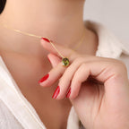 Gold necklace with a green gemstone perdiot pendant held by a hand with red nail polish.