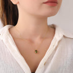 Close-up of a person wearing a gold necklace with an oval green peridot pendant.