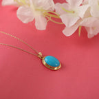 Gold necklace with a blue pendant on a pink background with flowers
