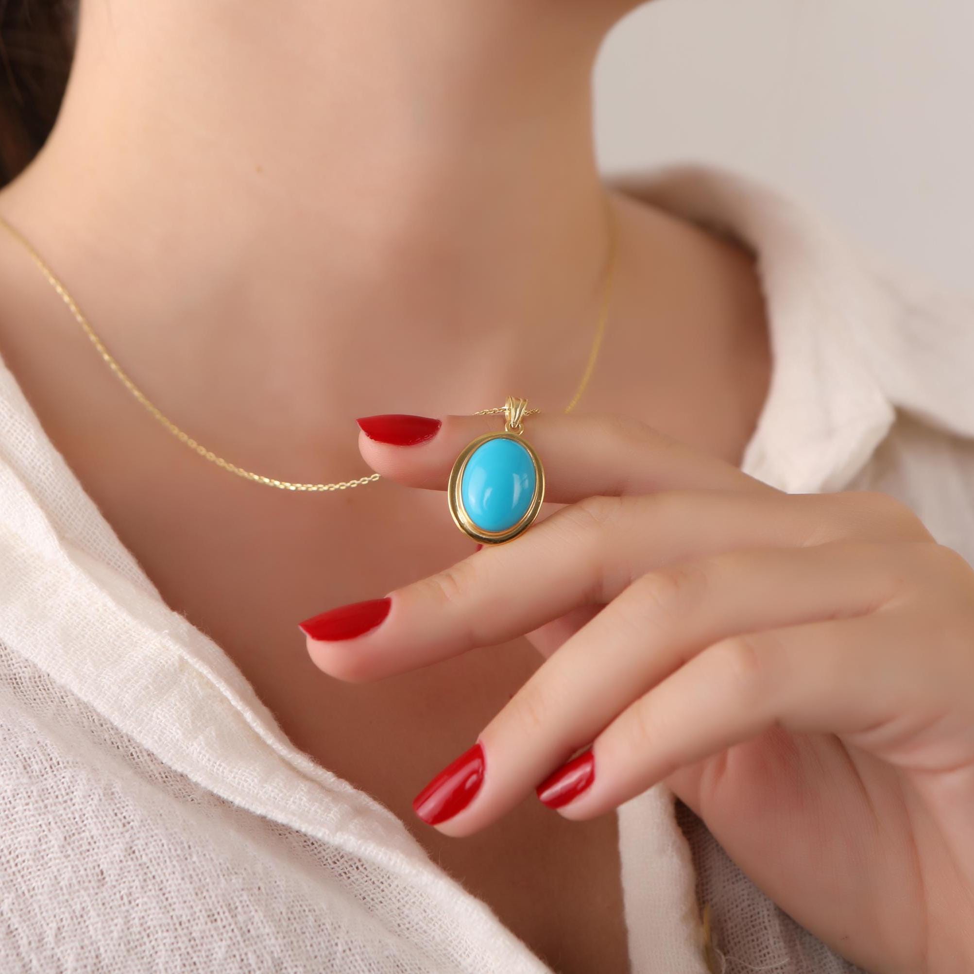 Woman wearing a gold necklace with a turquoise pendant, close-up of the necklace.