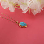 Gold necklace with a turquoise pendant on a pink background