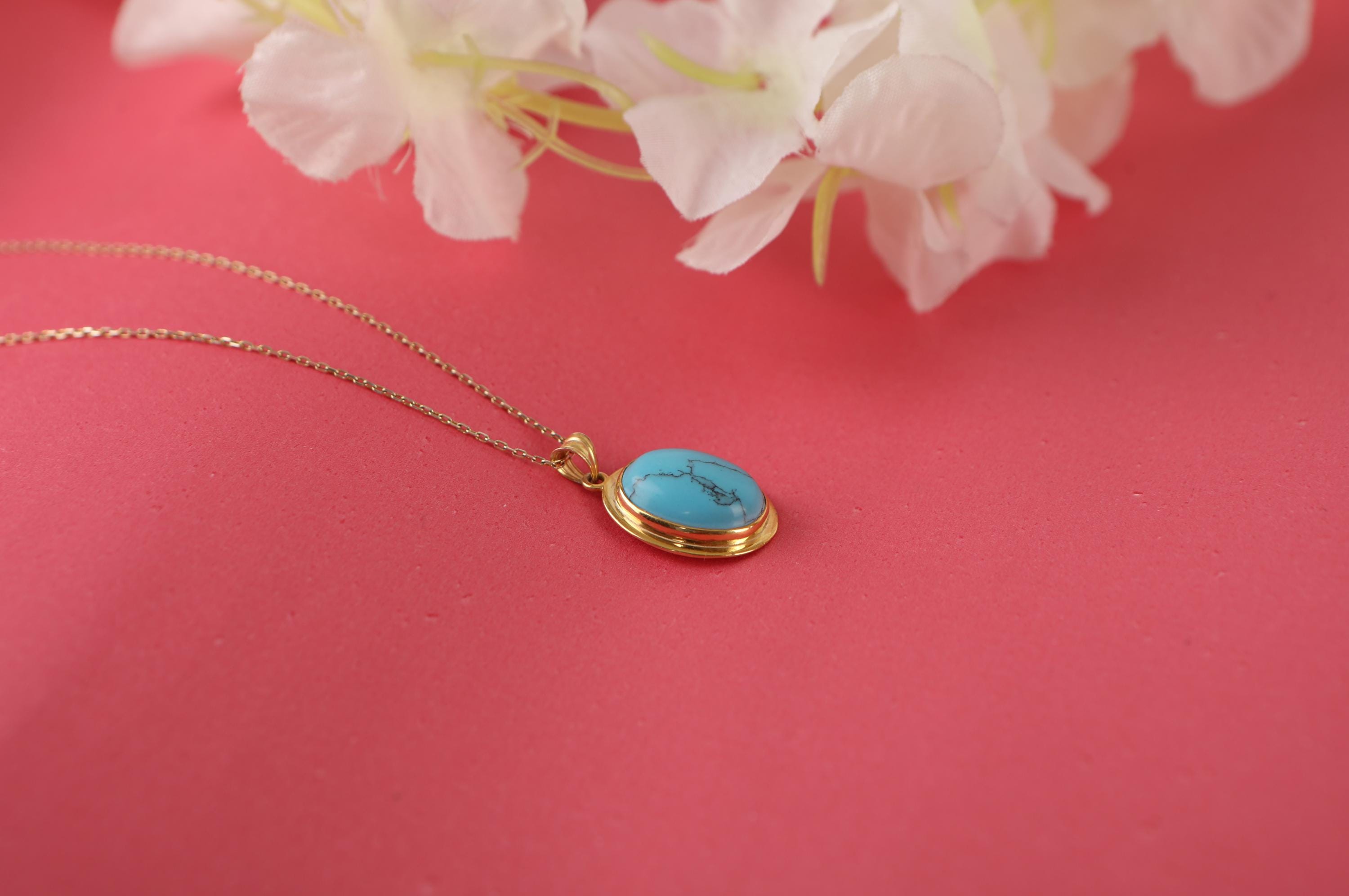 Gold necklace with a turquoise pendant on a pink background