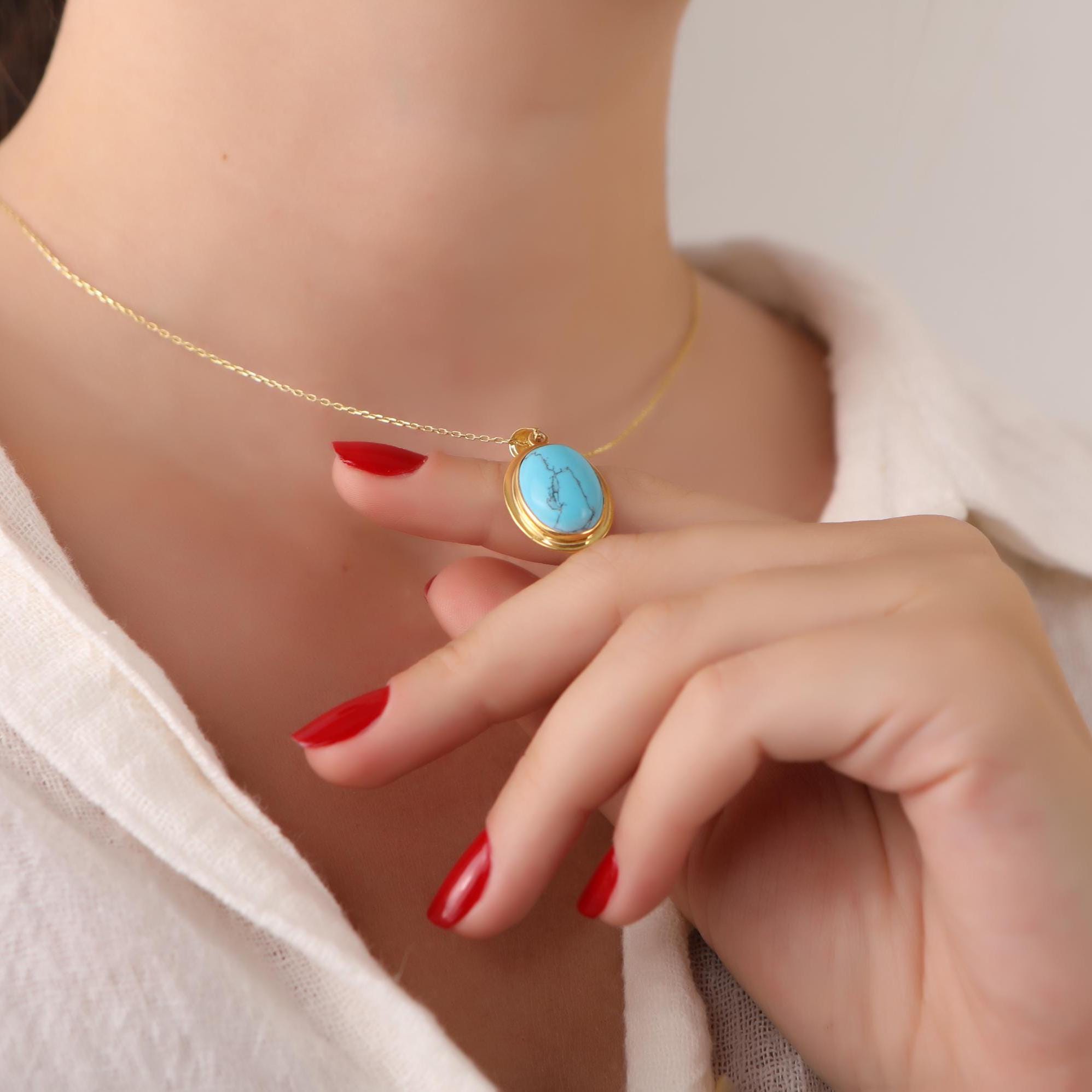 Close-up of a person wearing a gold necklace with a turquoise pendant, hand resting on shoulder.