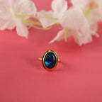 Gold ring with an abalone stone on a pink background with white flowers