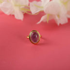 Gold ring with an amethyst gemstone on a red background with flowers