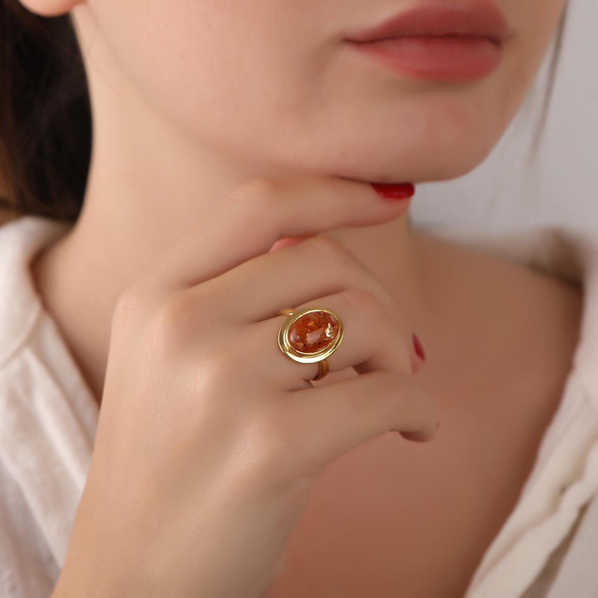 Close-up of a woman's hand wearing a gold ring with a red stone, touching her chin.