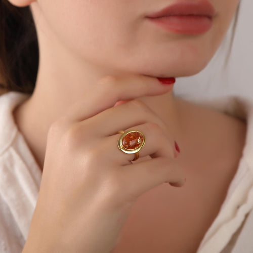 Close-up of a woman's hand wearing a gold ring with a red stone, touching her chin.