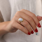 Hand wearing a gold ring with a circular agate stone, against a neutral background