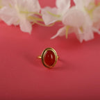 Gold bezel ring with a red stone on a pink background with white flowers