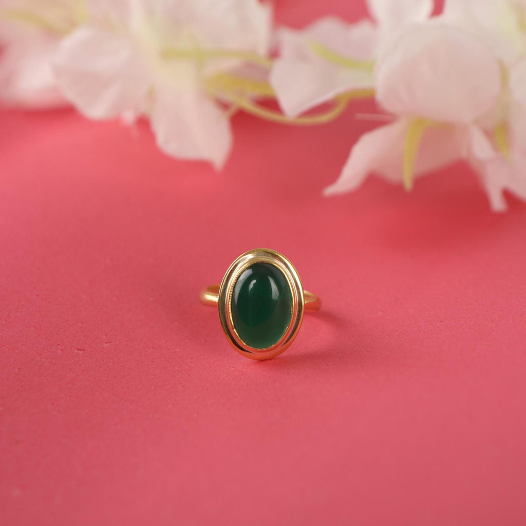 Gold ring with a green gemstone on a pink background with flowers