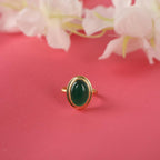Gold ring with a green gemstone on a pink background with flowers