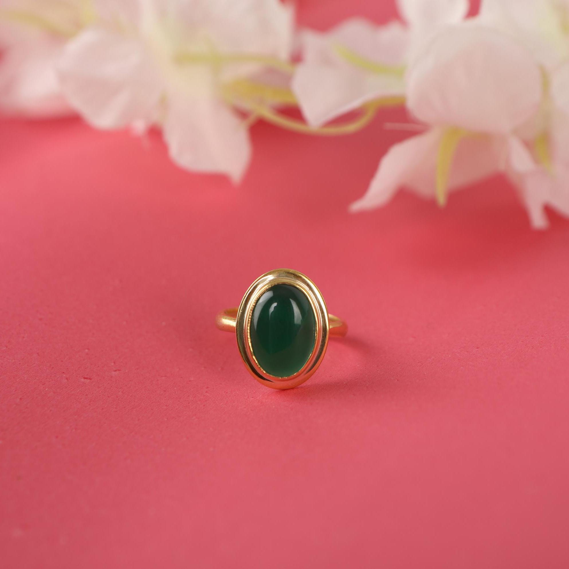 Gold ring with a green gemstone on a pink background with flowers