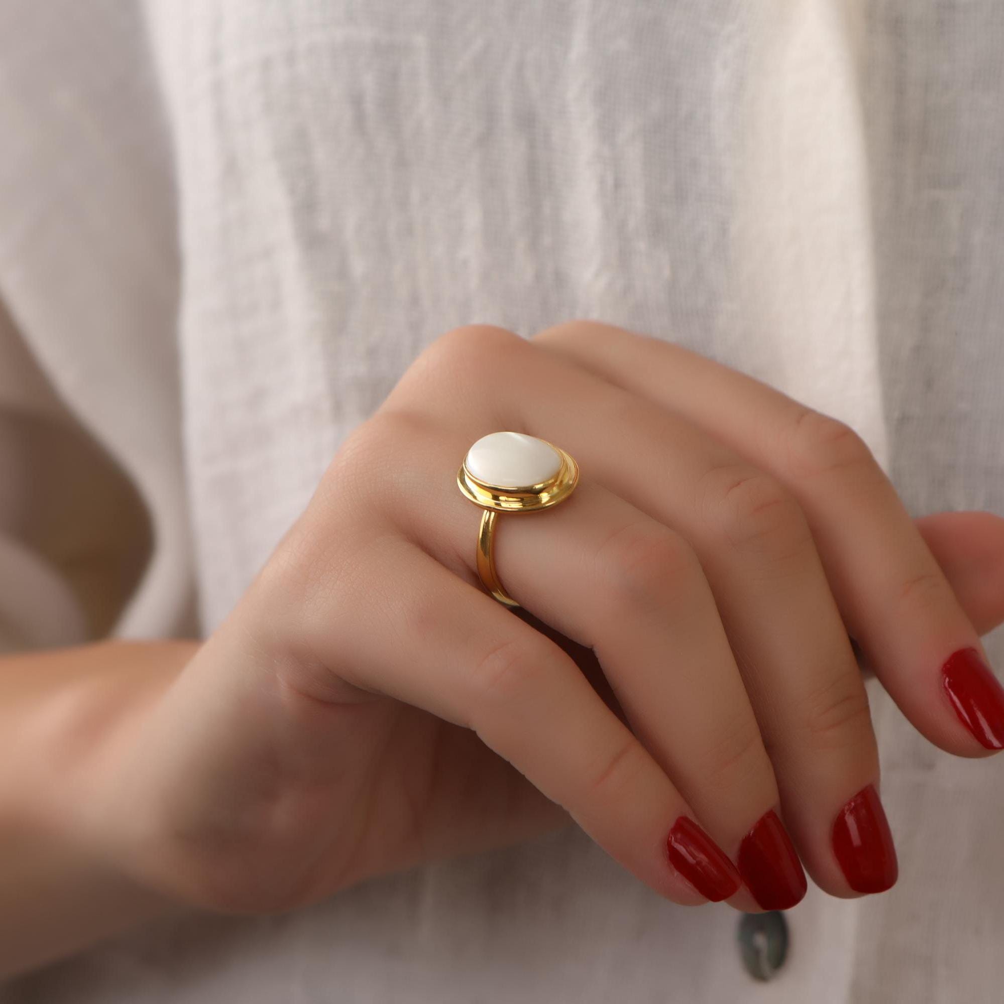 Hand wearing a gold ring with a white stone on a neutral background