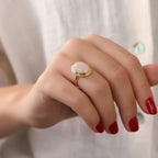 Hand wearing a gold ring with a pink stone against a neutral background