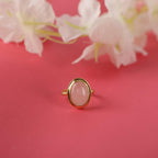Gold ring with a pink gemstone on a pink background with flowers
