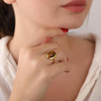 Close-up of a woman's hand wearing a gold ring with a tiger's eye stone, against a neutral background.