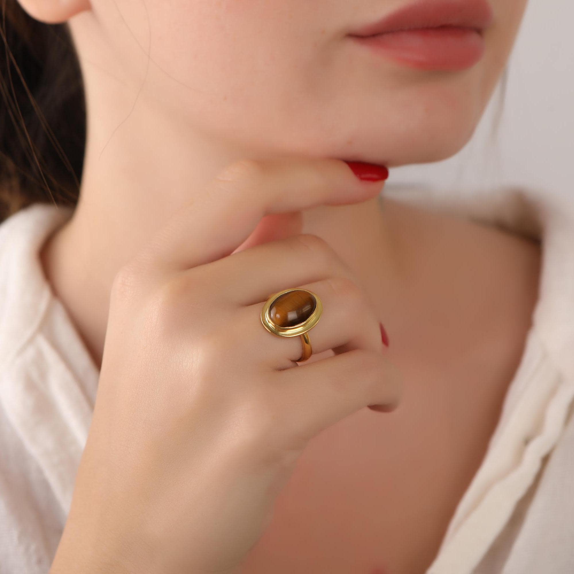 Close-up of a woman's hand wearing a gold ring with a tiger's eye stone, against a neutral background.