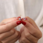 Pink tourmaline gemstone stud earrings held between fingers against a neutral background