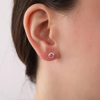 Close-up of an ear wearing a pink tourmaline stud earring against a neutral background