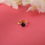 Gold ring with a blue gemstone on a pink background with flowers.
