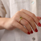 Hand wearing a gold ring with a green gemstone against a neutral background