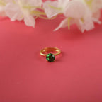 Gold ring with a round green gemstone on a pink background with flowers.