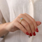 Hand wearing a gold ring with a blue gemstone against a white background