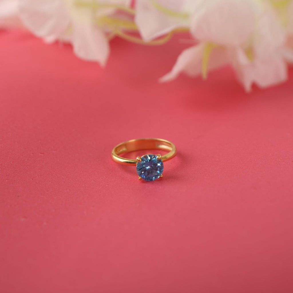 Gold ring with a blue gemstone on a pink background with white flowers.