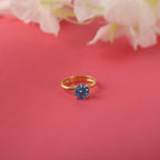 Gold ring with a blue gemstone on a pink background with white flowers.