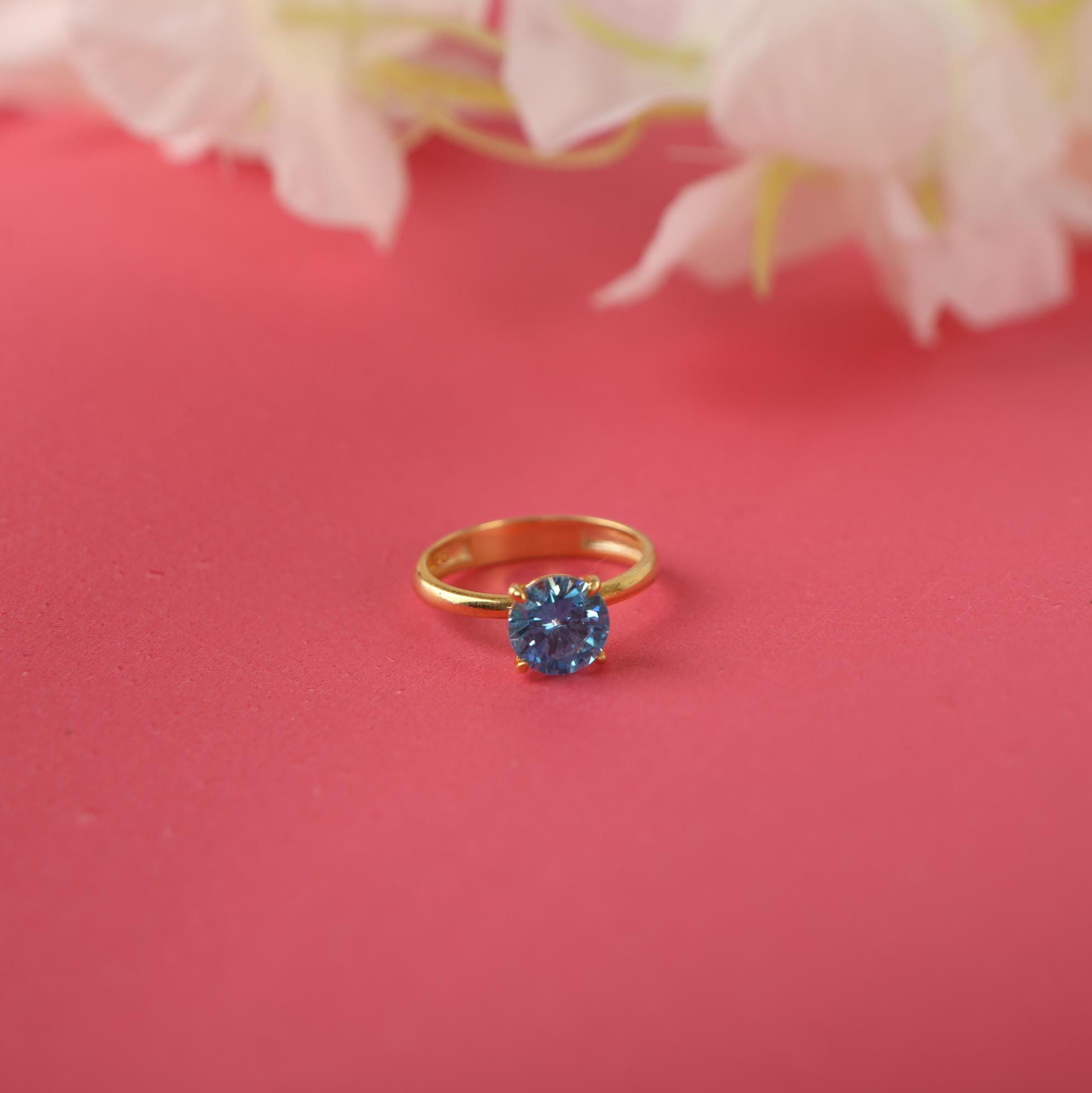 Gold ring with a blue gemstone on a pink background with white flowers.