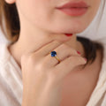 Close-up of a hand wearing a gold ring with a blue gemstone, blurred background