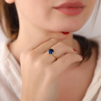Close-up of a hand wearing a gold ring with a blue gemstone, blurred background