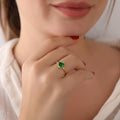 Close-up of a hand wearing a gold ring with a green gemstone, blurred background