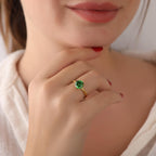 Close-up of a hand wearing a gold ring with a green gemstone, blurred background