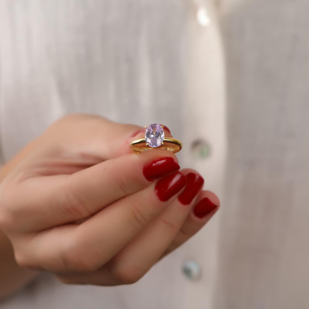 Hand holding a ring with a purple gemstone against a neutral background