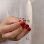 Hand holding a ring with a purple gemstone against a neutral background
