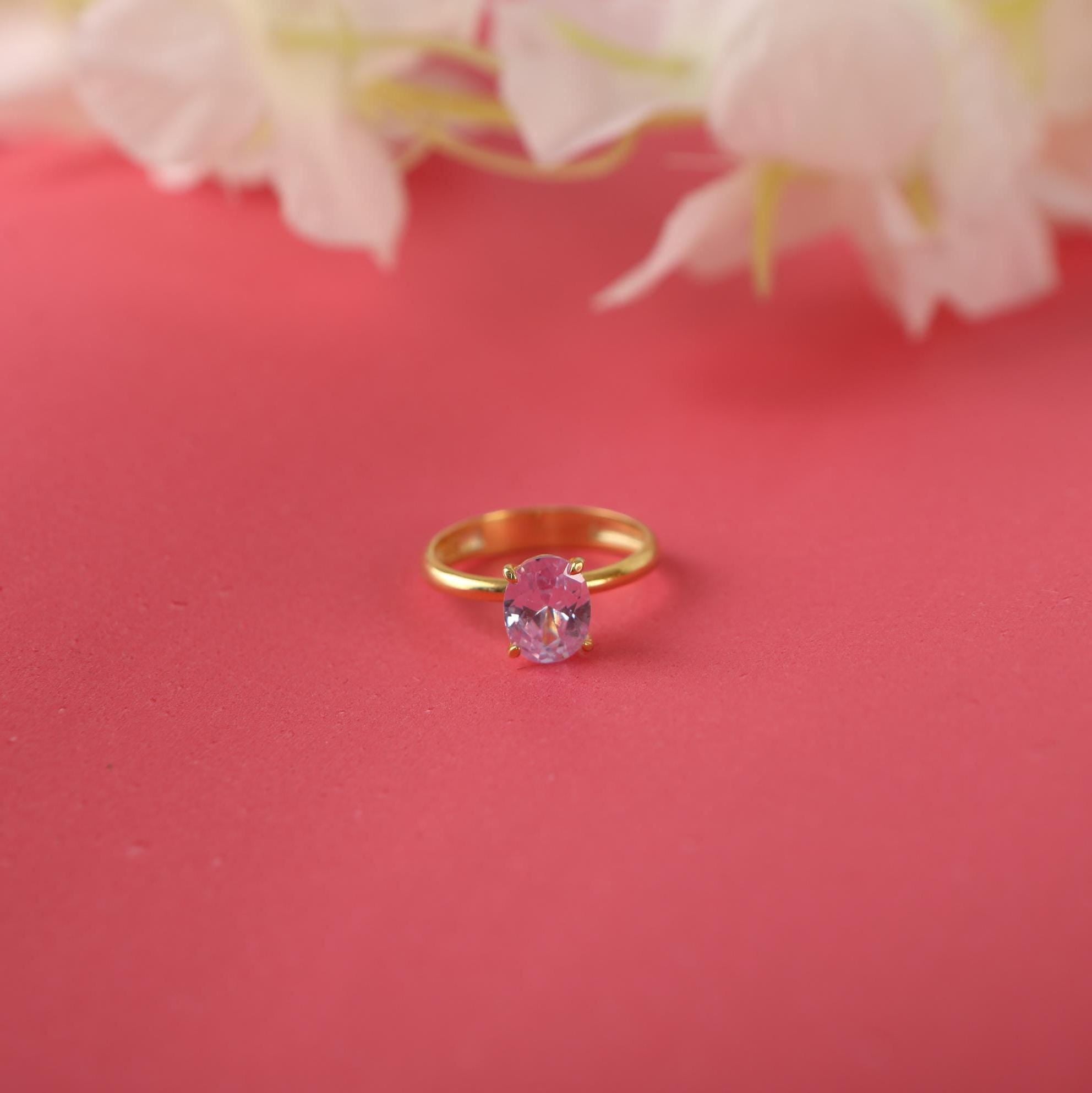 Gold ring with a pink gemstone on a red background with flowers.