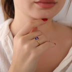 Close-up of a hand wearing a gold ring with a purple gemstone, touching the lips.