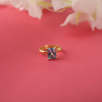 Gold ring with a rectangular gemstone on a pink background with flowers.