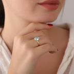 Close-up of a hand wearing a gold ring with a blue gemstone, against a neutral background.