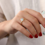 Hand wearing a gold ring with a clear gemstone on a neutral background
