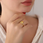 Close-up of a hand wearing a gold ring with a yellow gemstone, against a neutral background.